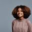 Minimal portrait of young African-American woman with natural curly hair smiling at camera against blue background, copy space